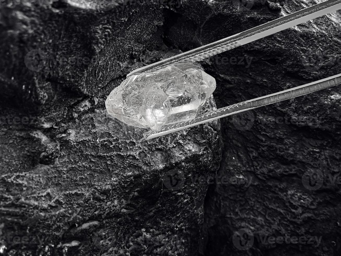 diamante natural mantido em pinças em fundo preto de carvão foto