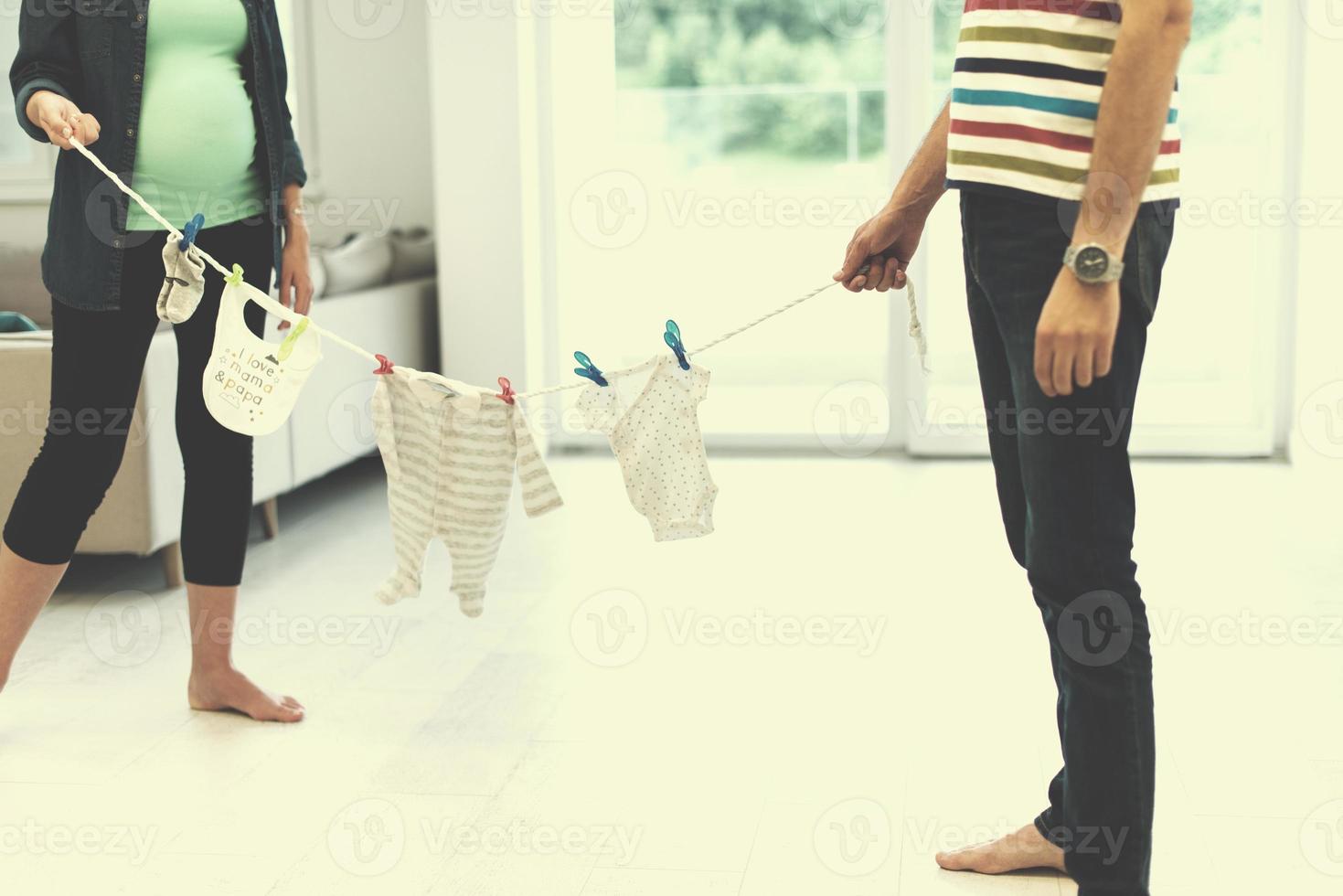 jovem casal segurando roupas de bebê em casa foto