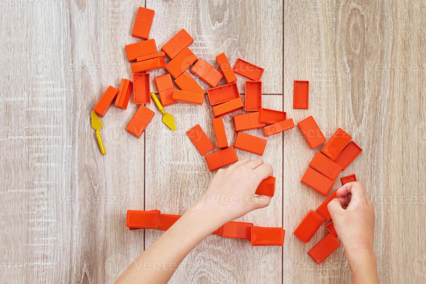 vista superior das mãos de criança brincando com tijolos de brinquedo laranja foto