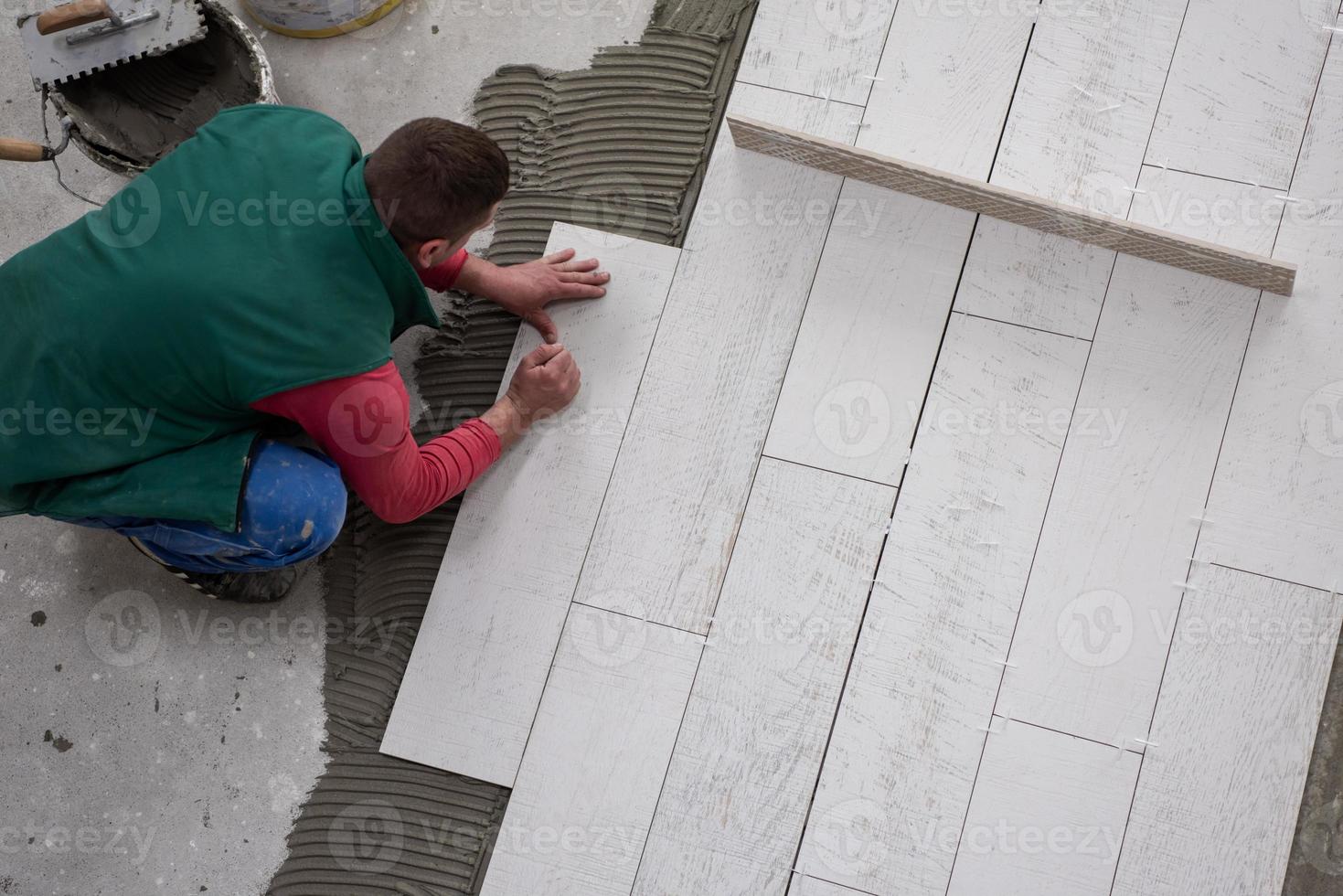 trabalhador instalando as telhas cerâmicas de efeito de madeira no chão foto