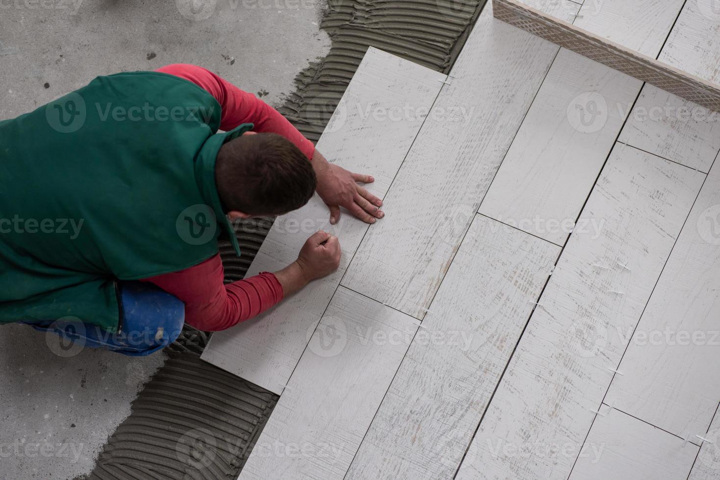 trabalhador instalando as telhas cerâmicas de efeito de madeira no chão foto