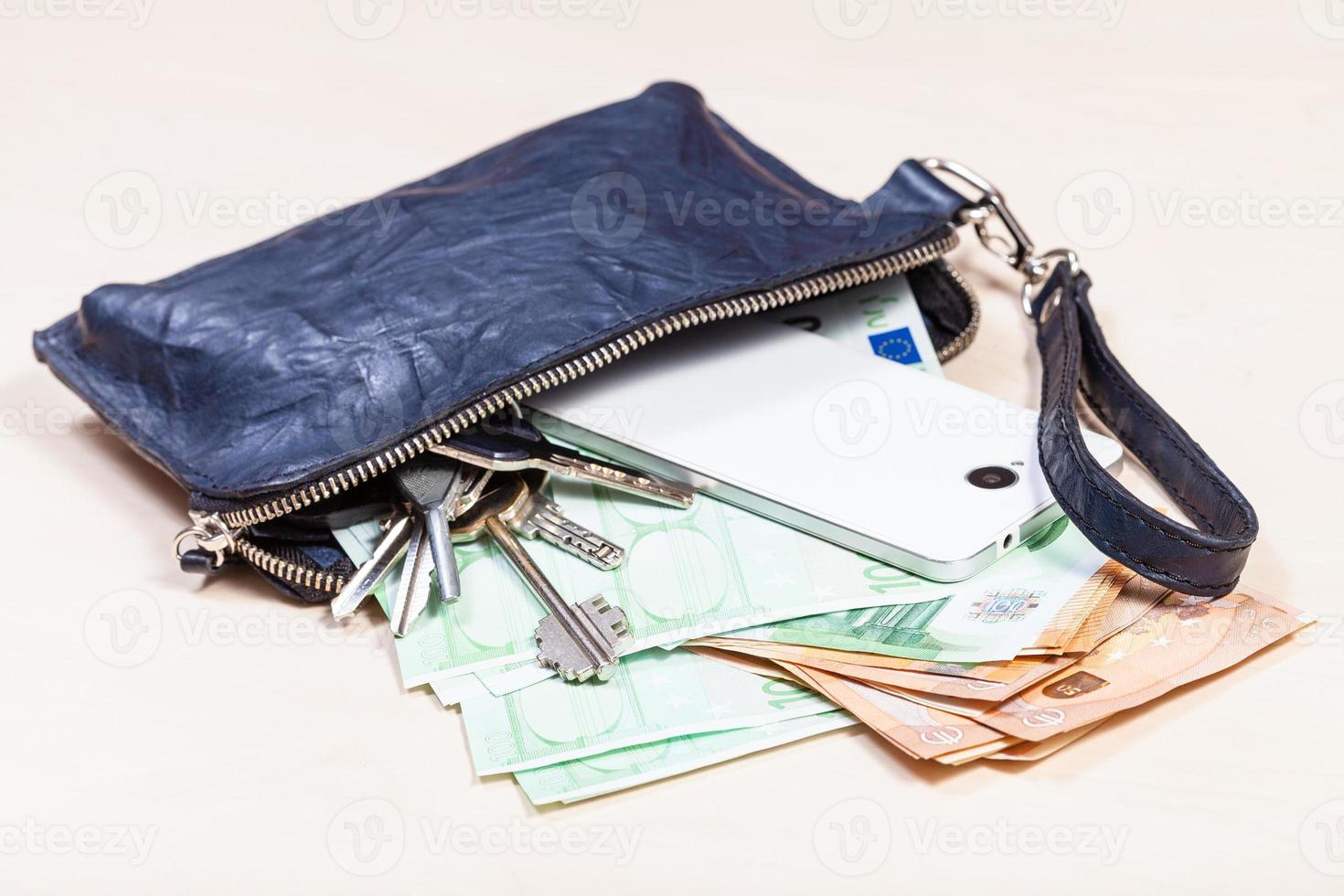 bolsa com telefone, chaves e muitos euros na mesa foto