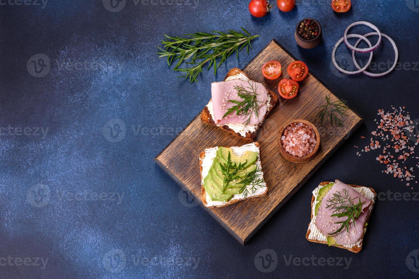 sanduíches frescos e deliciosos de presunto, manteiga, abacate e sementes de gergelim em uma tábua de madeira foto