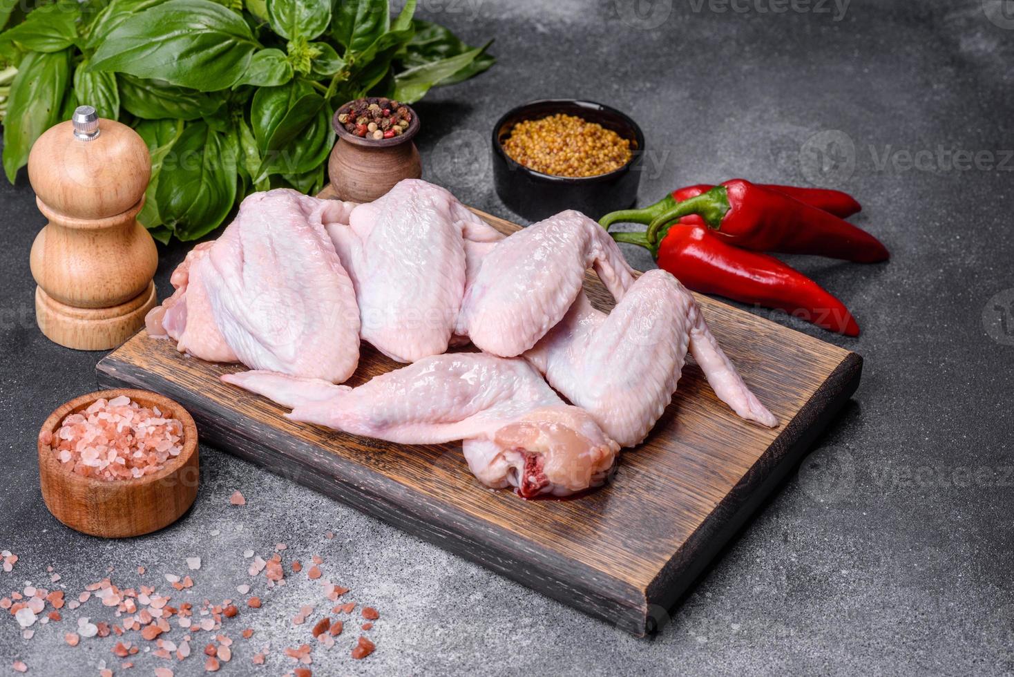 asas de frango cru com ingredientes para cozinhar em uma tábua de madeira foto