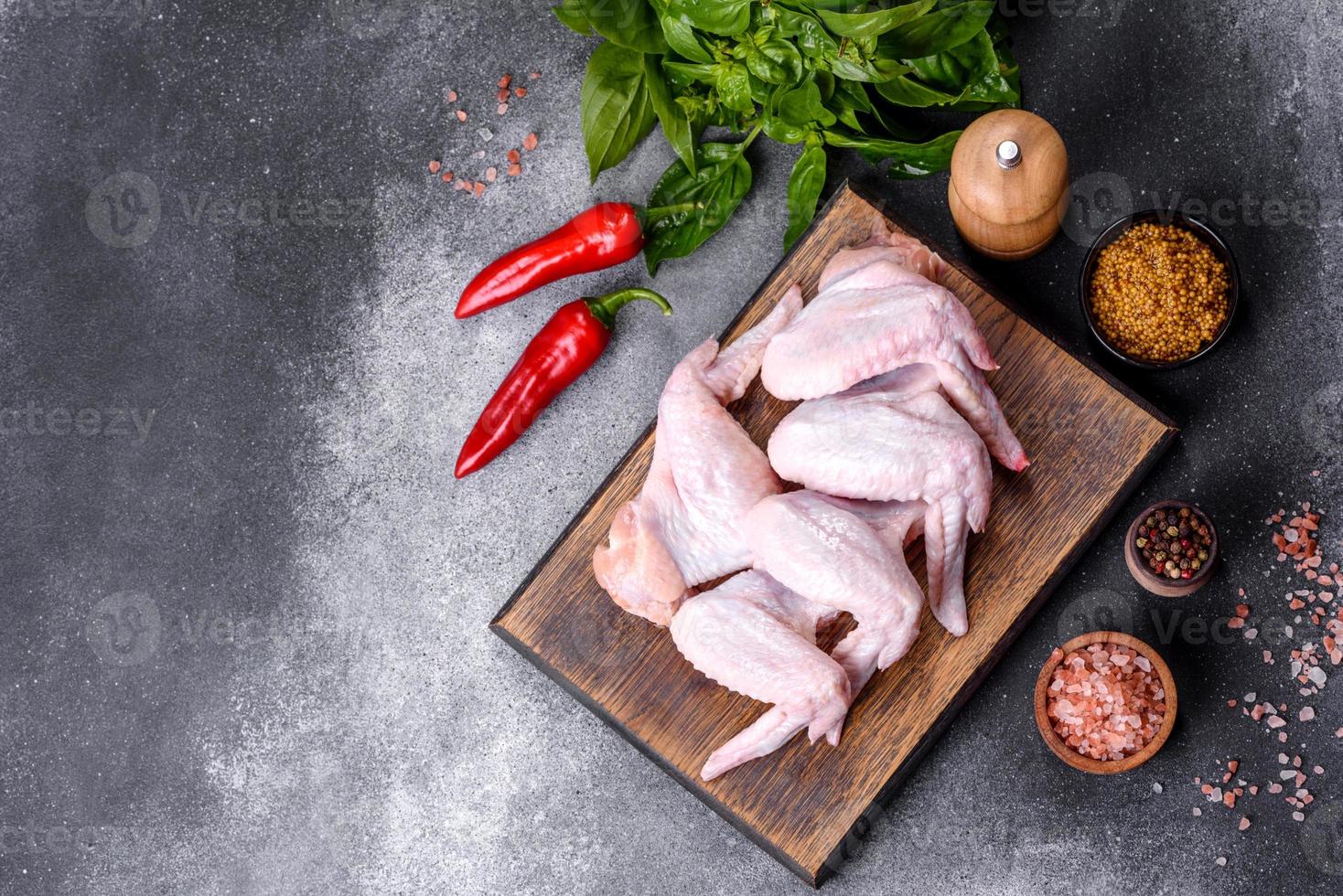asas de frango cru com ingredientes para cozinhar em uma tábua de madeira foto