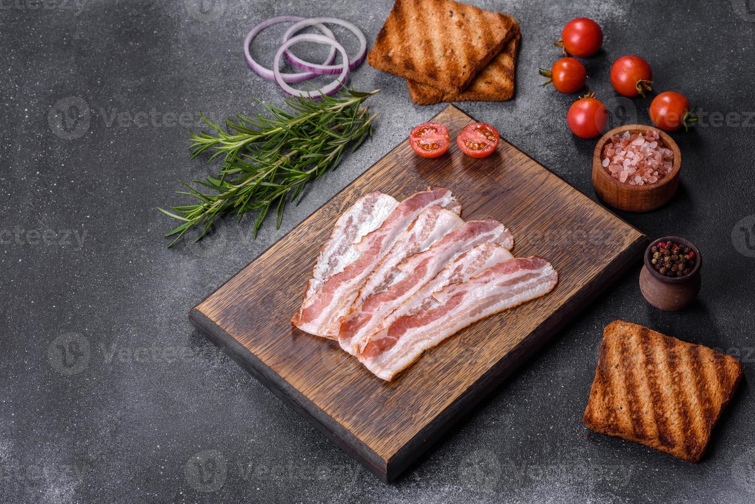 fatias de bacon defumado cru em uma placa de madeira com especiarias e ervas foto