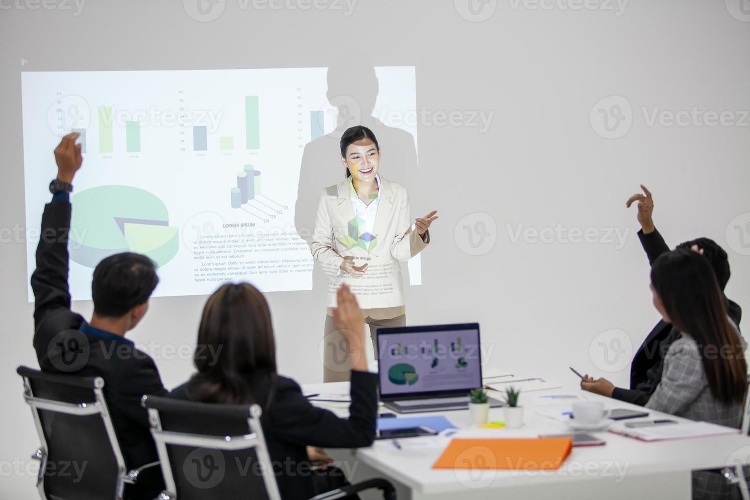 equipe de negócios asiáticos colegas masculinos e femininos conversando no trabalho compartilham ideias com gráfico a bordo, colegas levantaram as mãos para a pergunta. foto