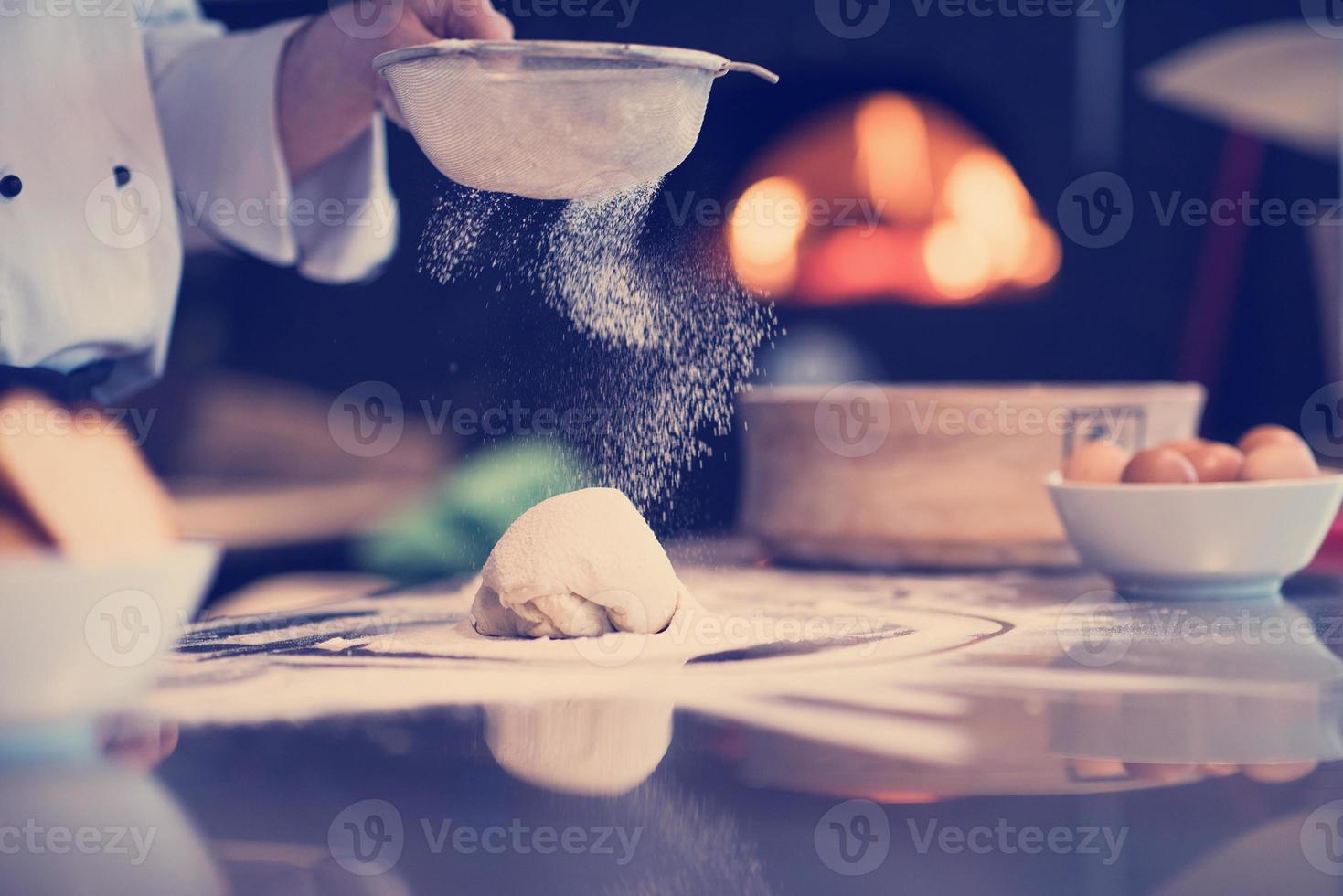 chef polvilhando farinha sobre a massa de pizza fresca foto
