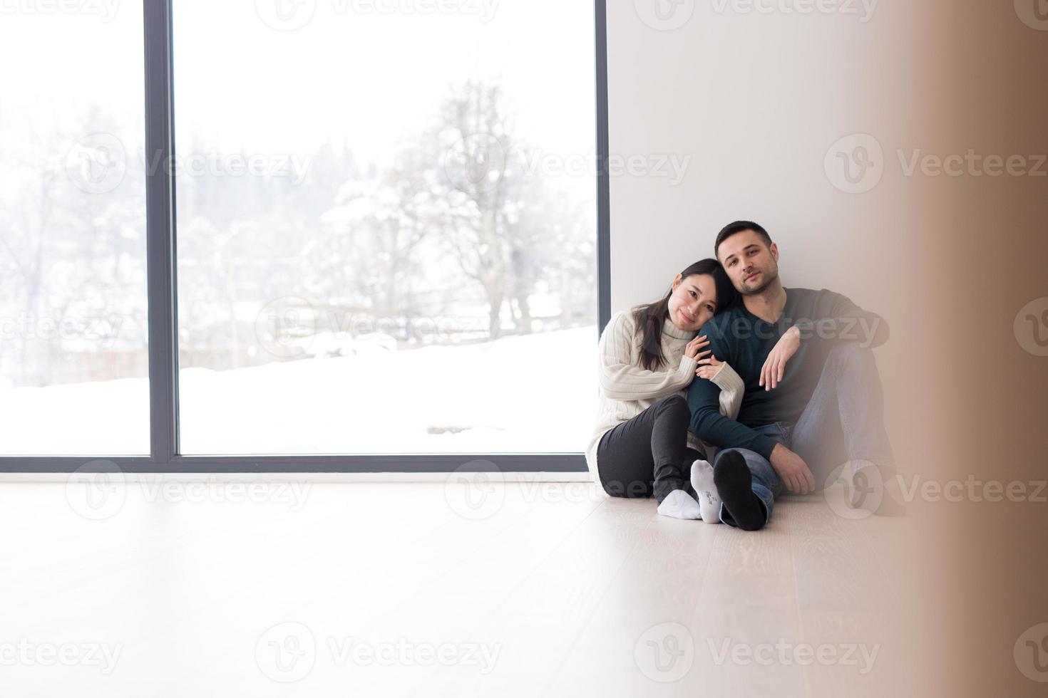 casal multiétnico sentado no chão perto da janela em casa foto