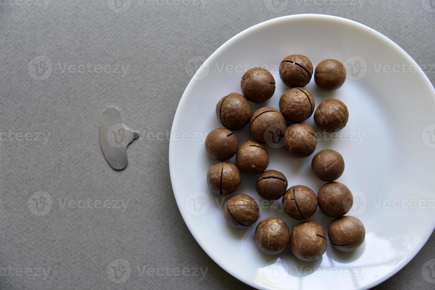 noz de macadâmia em um prato com um abridor de garrafas em um fundo cinza. macadâmia preparada para uso em vaso. delicioso café da manhã de nozes. foto