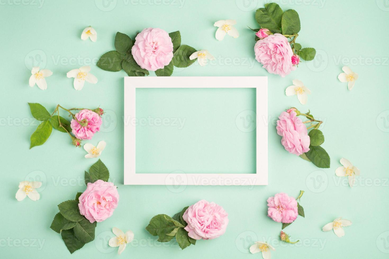 lindas flores rosas e moldura em branco sobre fundo pastel de hortelã. cor clara suave. vista superior, copie o espaço foto