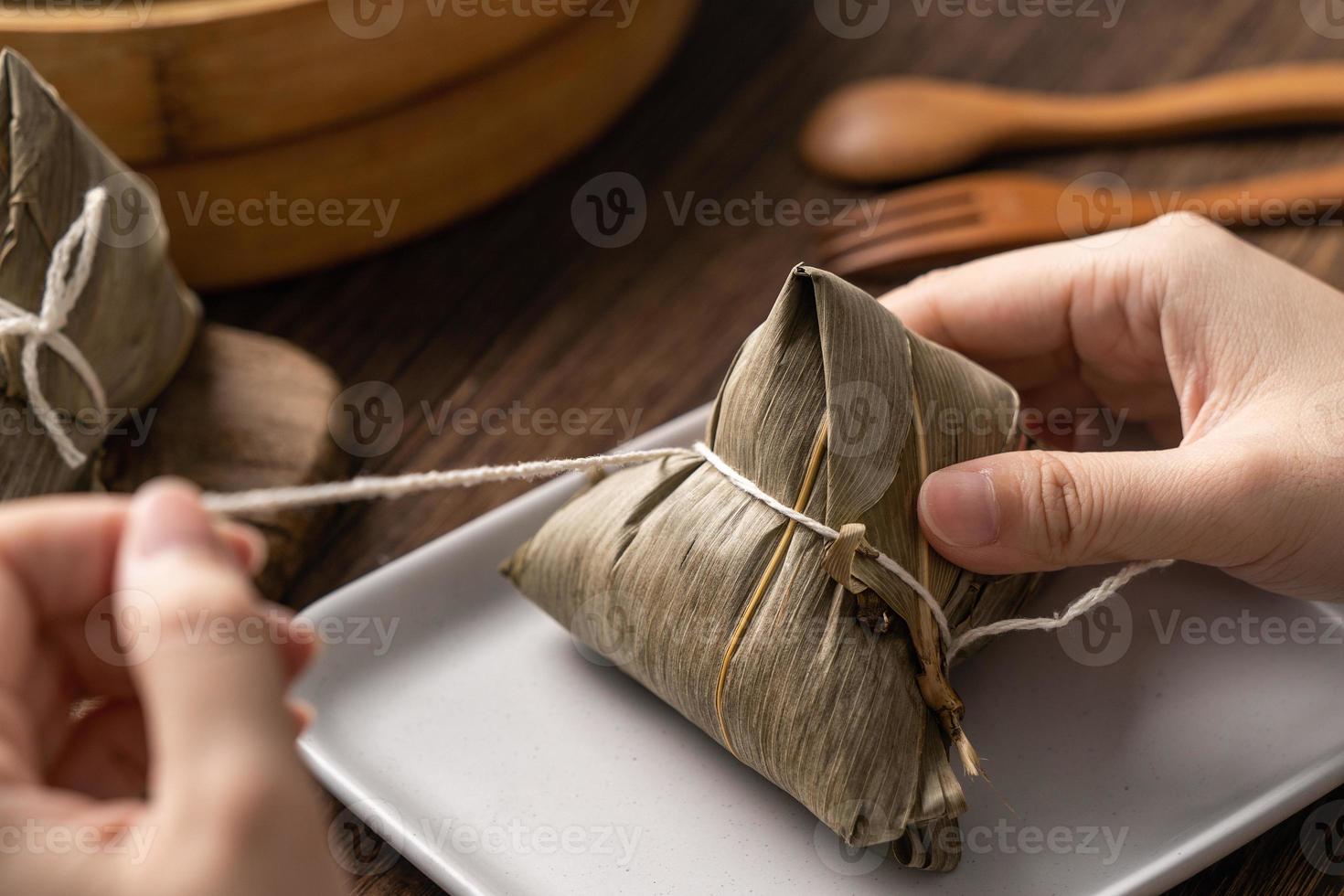 bolinho de arroz zongzi comendo - jovem asiática está comendo comida tradicional chinesa na mesa de madeira em casa para a celebração do festival do barco dragão, close-up foto