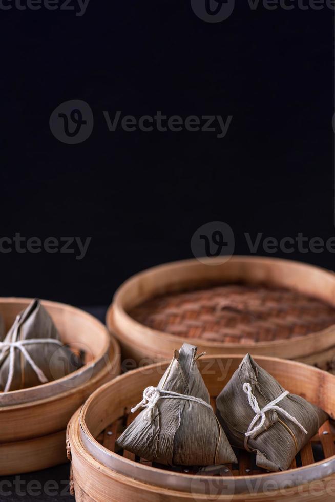 bolinho de arroz, zongzi - festival de barco de dragão, bando de comida tradicional chinesa cozida no vapor na mesa de madeira sobre fundo preto, close-up, copie o espaço foto