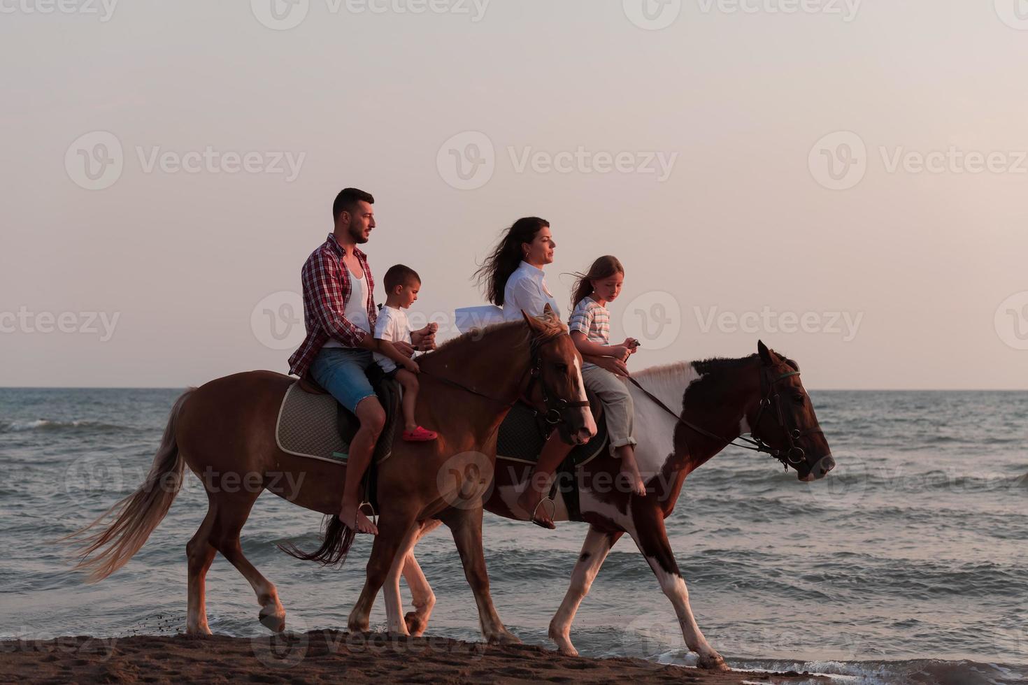 a família passa o tempo com seus filhos enquanto andam a cavalo juntos em uma praia de areia. foco seletivo foto