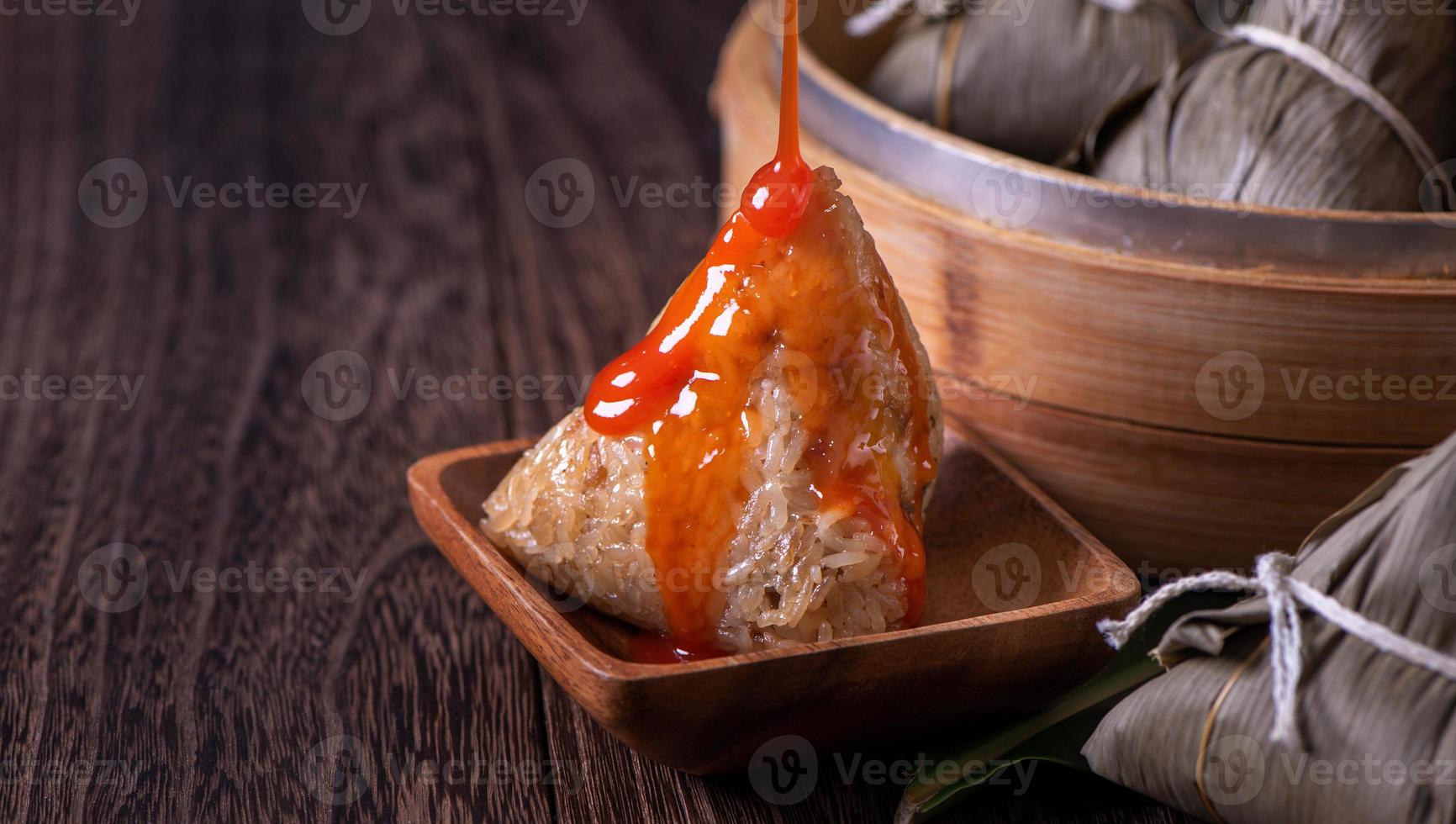 comida do festival do barco dragão - bolinho de arroz zongzi, jovem asiática comendo comida tradicional chinesa na mesa de madeira em casa celebração, close-up foto