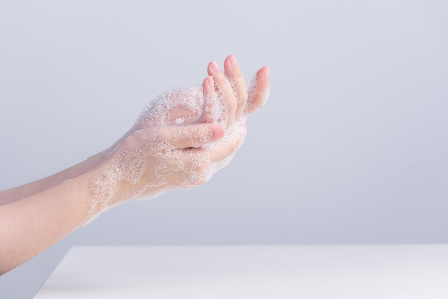 Lavando as mãos. jovem asiática usando sabão líquido para lavar as mãos, conceito de higiene para proteger o coronavírus pandêmico isolado em fundo branco cinza, close-up. foto