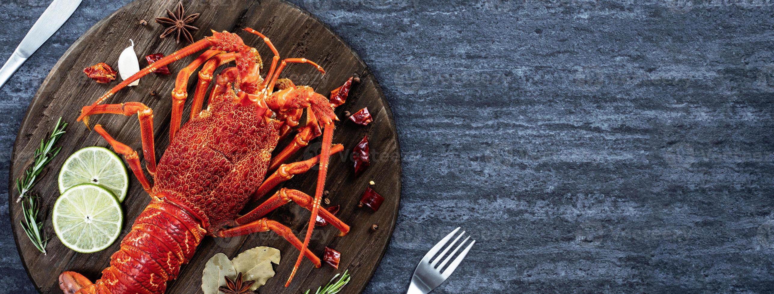 lagosta cozida cozida, deliciosa refeição de frutos do mar jantar com faca e garfo em fundo de ardósia de pedra preta, design de menu de restaurante, vista superior, sobrecarga foto