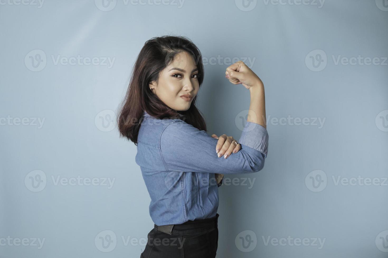 mulher asiática animada, vestindo uma camisa azul, mostrando um gesto forte, levantando os braços e os músculos sorrindo orgulhosamente foto