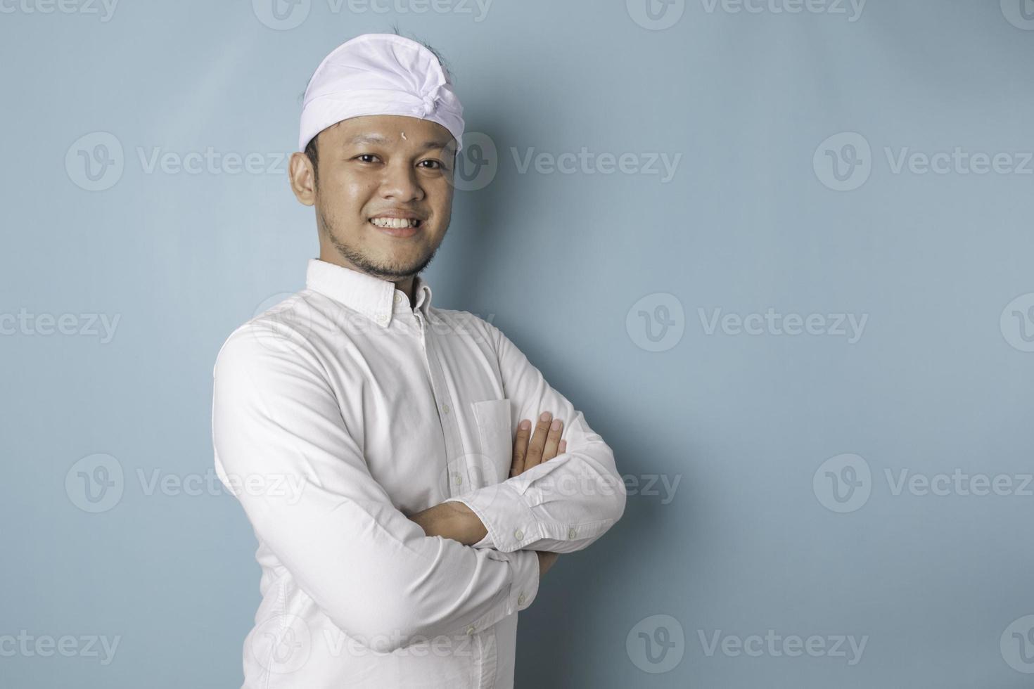 retrato de um homem balinês sorridente confiante em pé com os braços cruzados e olhando para a câmera isolada sobre fundo azul, vestindo uma camisa azul foto