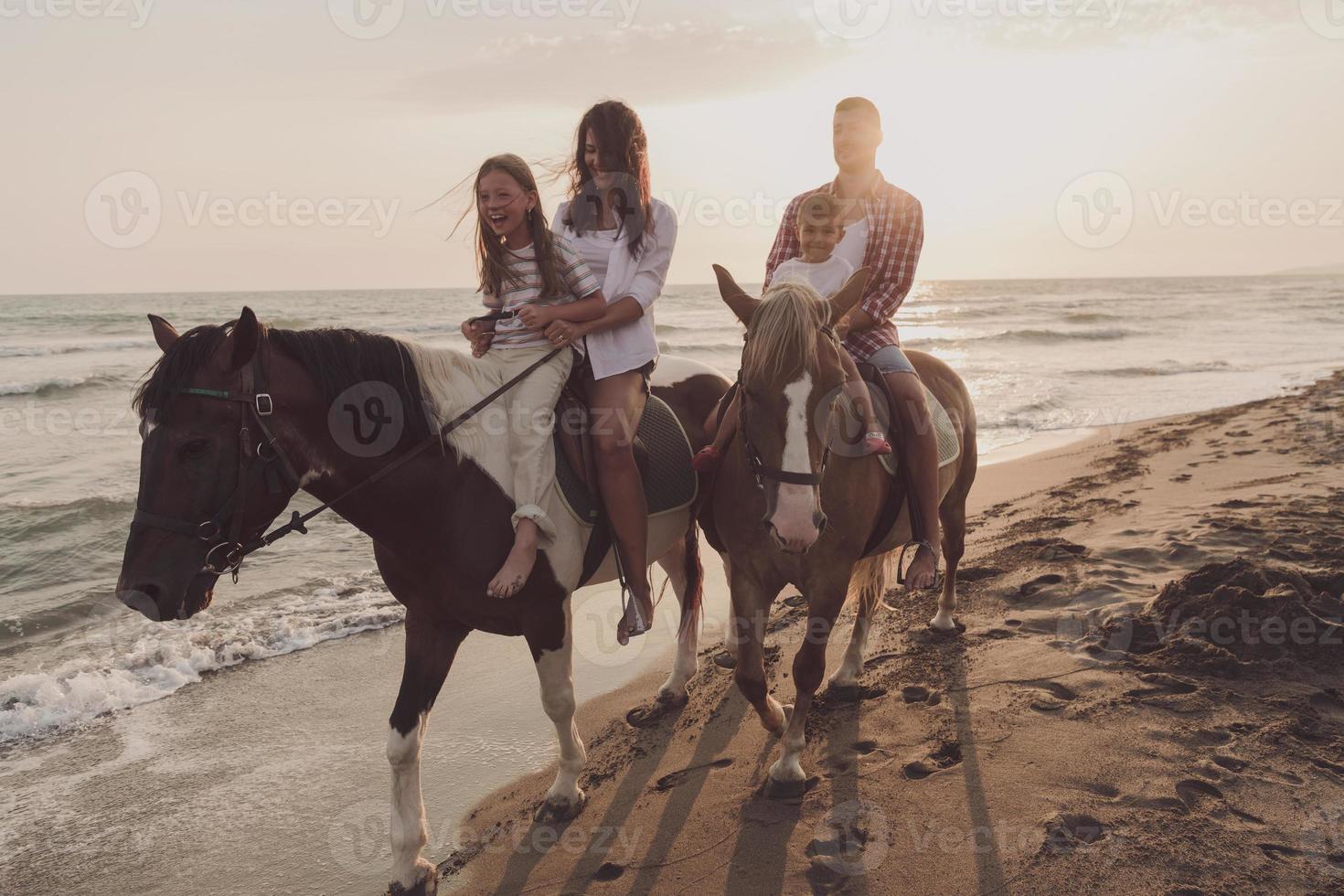 a família passa o tempo com seus filhos enquanto andam a cavalo juntos em uma bela praia de areia ao pôr do sol. foto