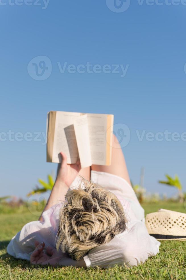 mulher mentindo e lendo seu livro favorito em um prado coberto de grama verde fresca em um dia ensolarado de verão ou primavera. foto