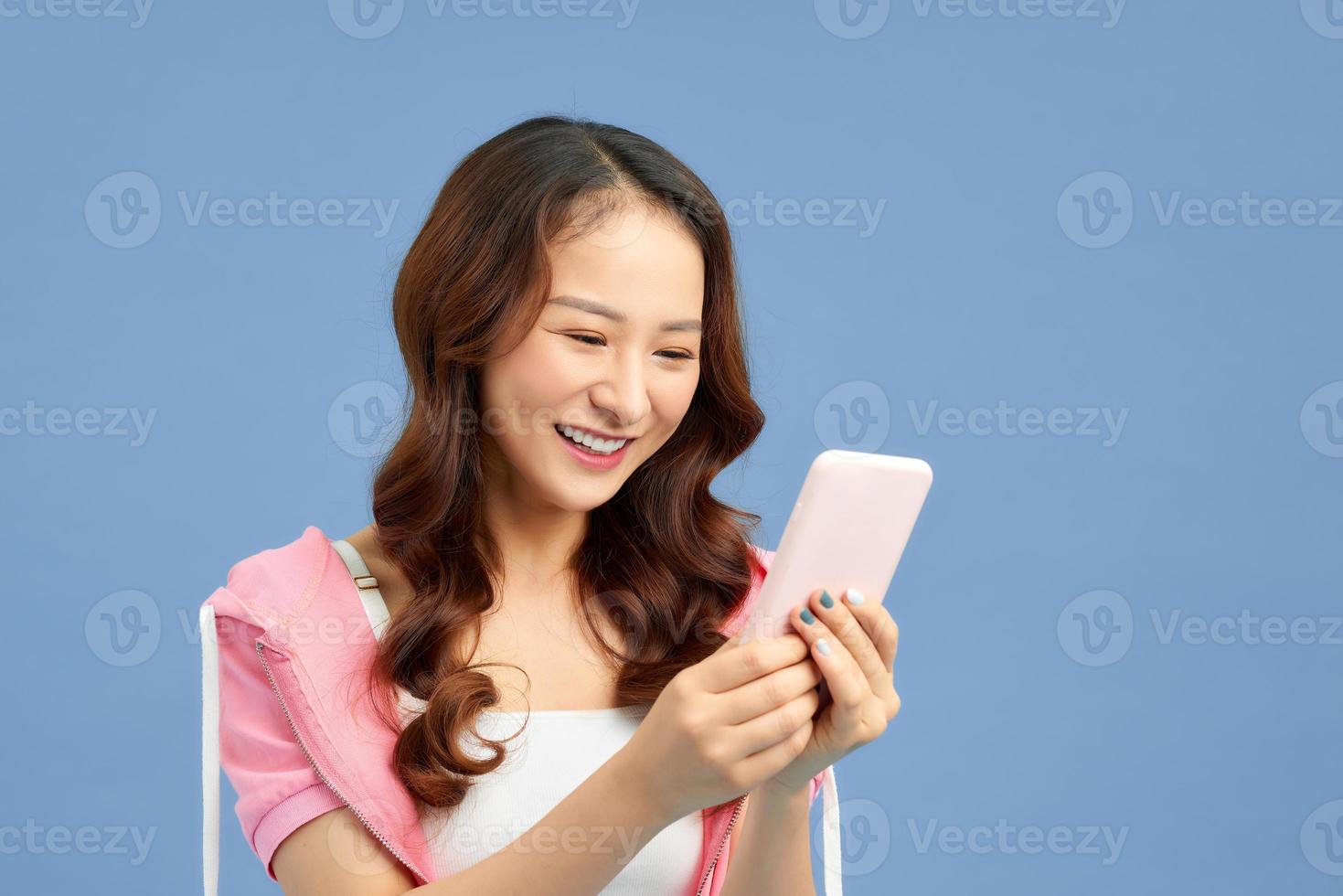 mensagem de mensagens de texto feliz jovem mulher asiática com seu fundo azul smartphone isolado. foto