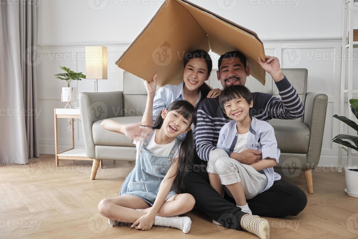 família tailandesa asiática, pai adulto, mãe e crianças pequenas brincando alegremente em uma sala de estar branca, casa de segurança de papelão construída com imaginação, fim de semana adorável e estilo de vida doméstico de bem-estar. foto