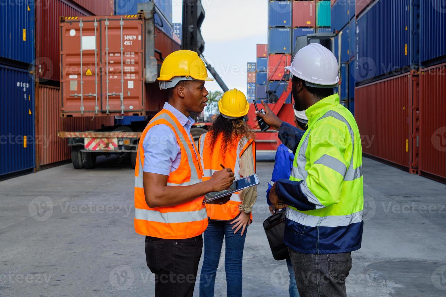 trabalhadores masculinos afro-americanos e equipes em uniformes de segurança e capacetes usam walkie-talkies, trabalham no guindaste logístico com pilhas de contêineres, mercadorias de transporte de controle de carga e indústria de transporte de carga. foto