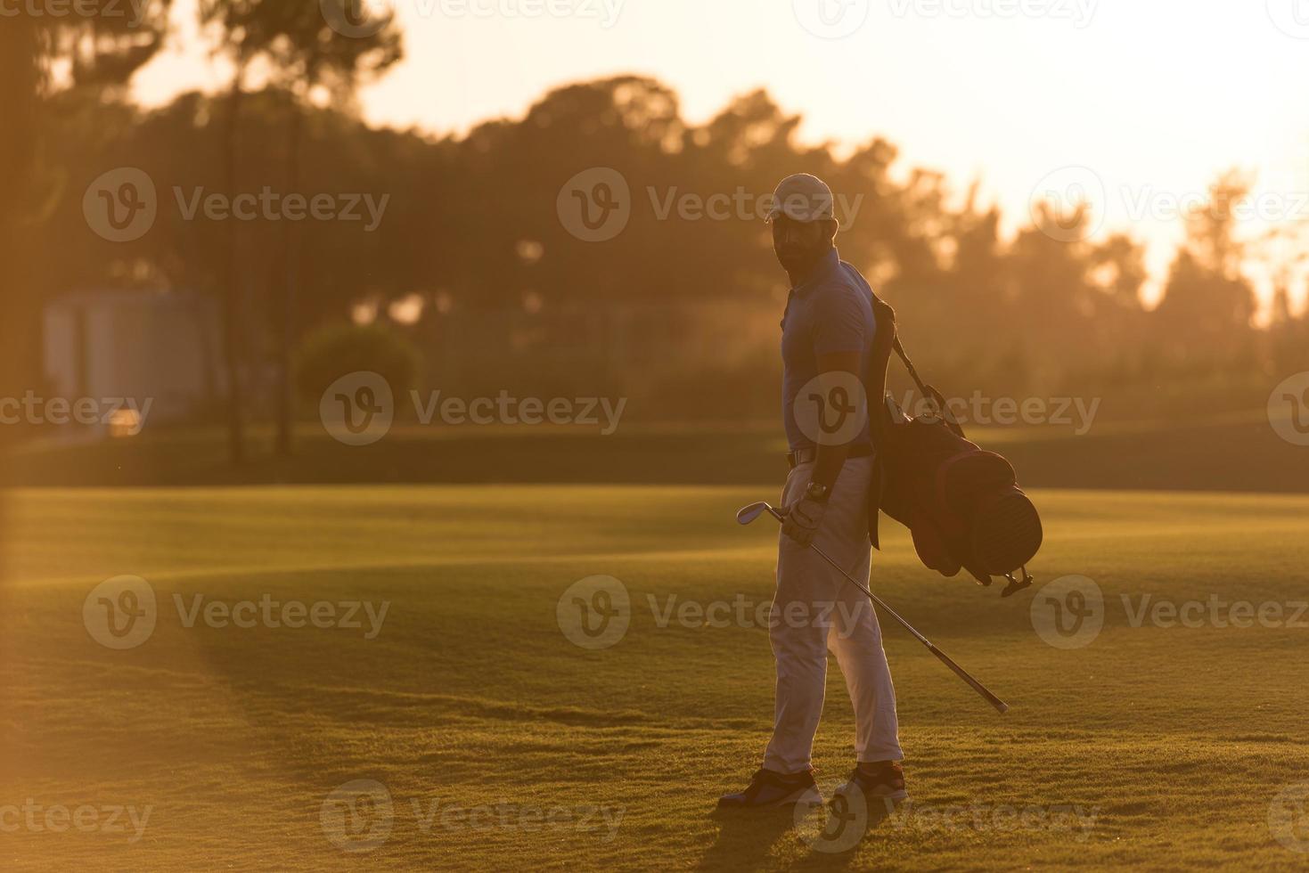 golfista andando e carregando saco de golfe no belo pôr do sol foto