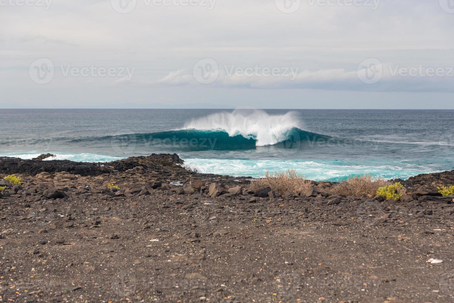 ondas oceânicas turbulentas com espuma branca batem nas pedras costeiras foto