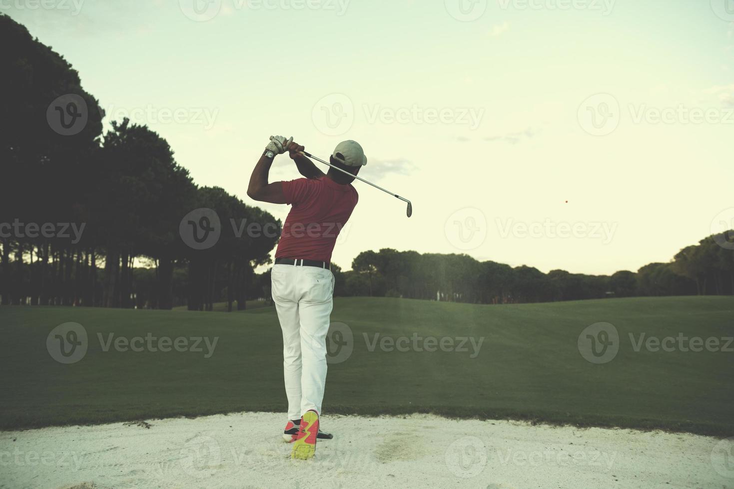 golfista acertando um bunker de areia no pôr do sol foto