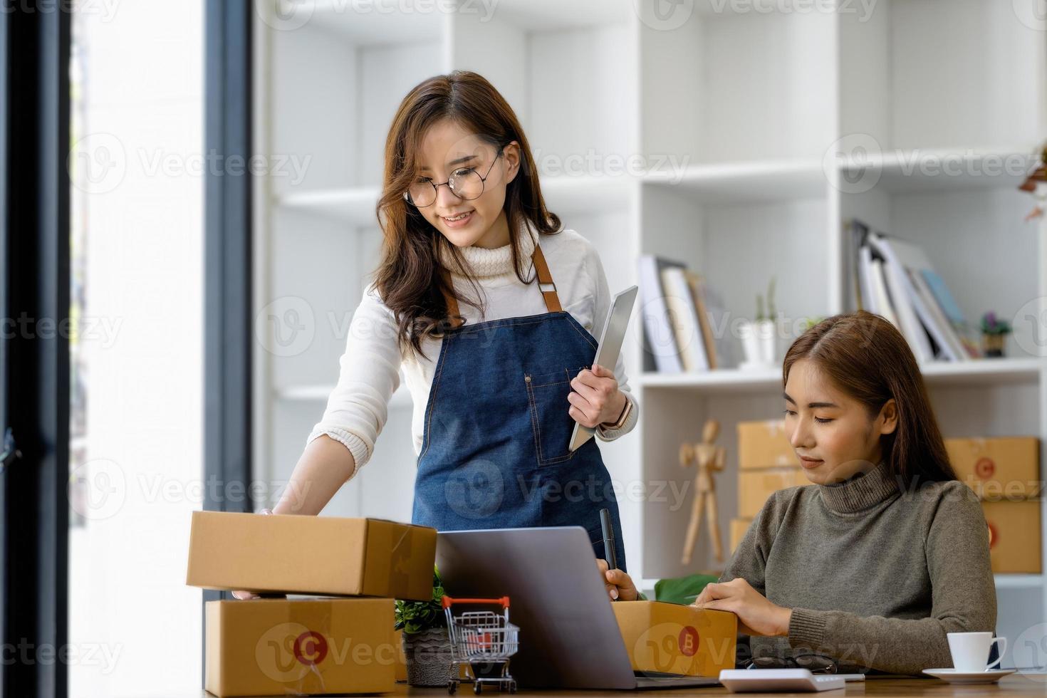 duas mulheres felizes vendendo produtos online. comece um pequeno empresário com uma caneta para anotar os endereços dos clientes e prepará-los para postagem. foto