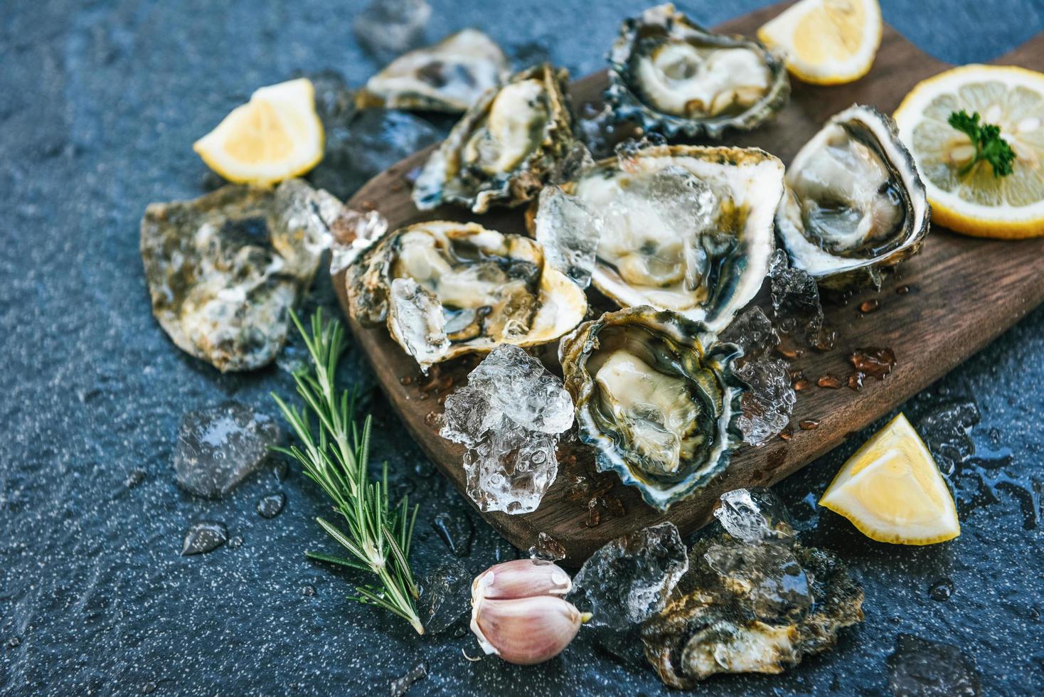 ostras frescas frutos do mar no fundo da placa de madeira - concha de ostra aberta com ervas especiarias limão alecrim servido mesa e gelo frutos do mar saudáveis jantar de ostras cruas no restaurante comida gourmet foto