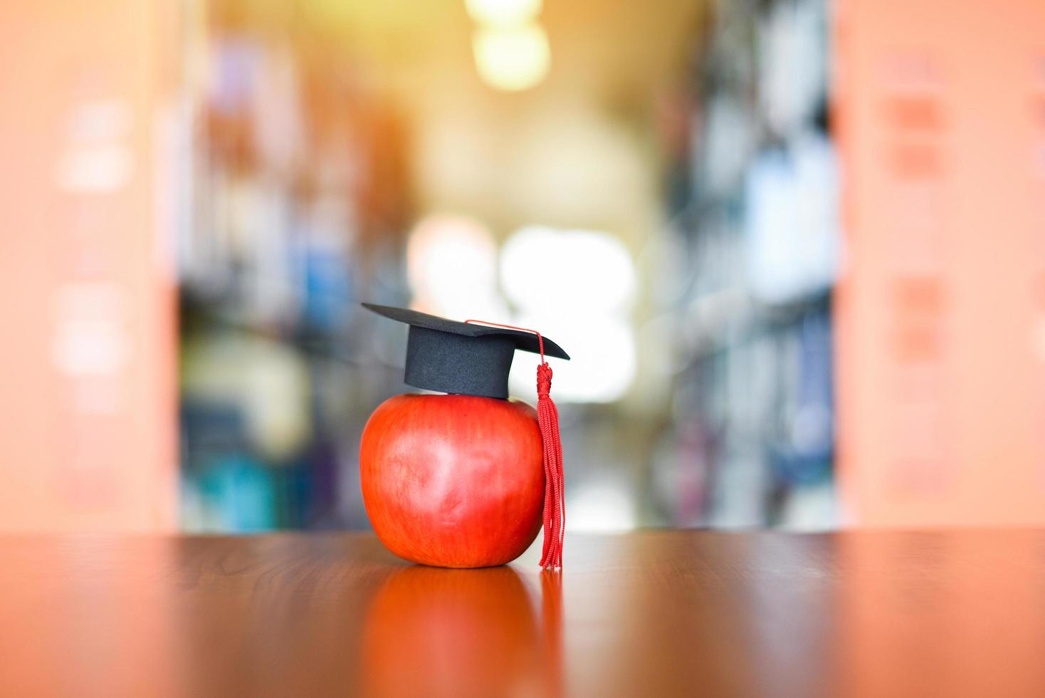 conceito de aprendizagem de educação - chapéu de formatura na maçã em cima da mesa com a estante de livros no fundo da biblioteca foto