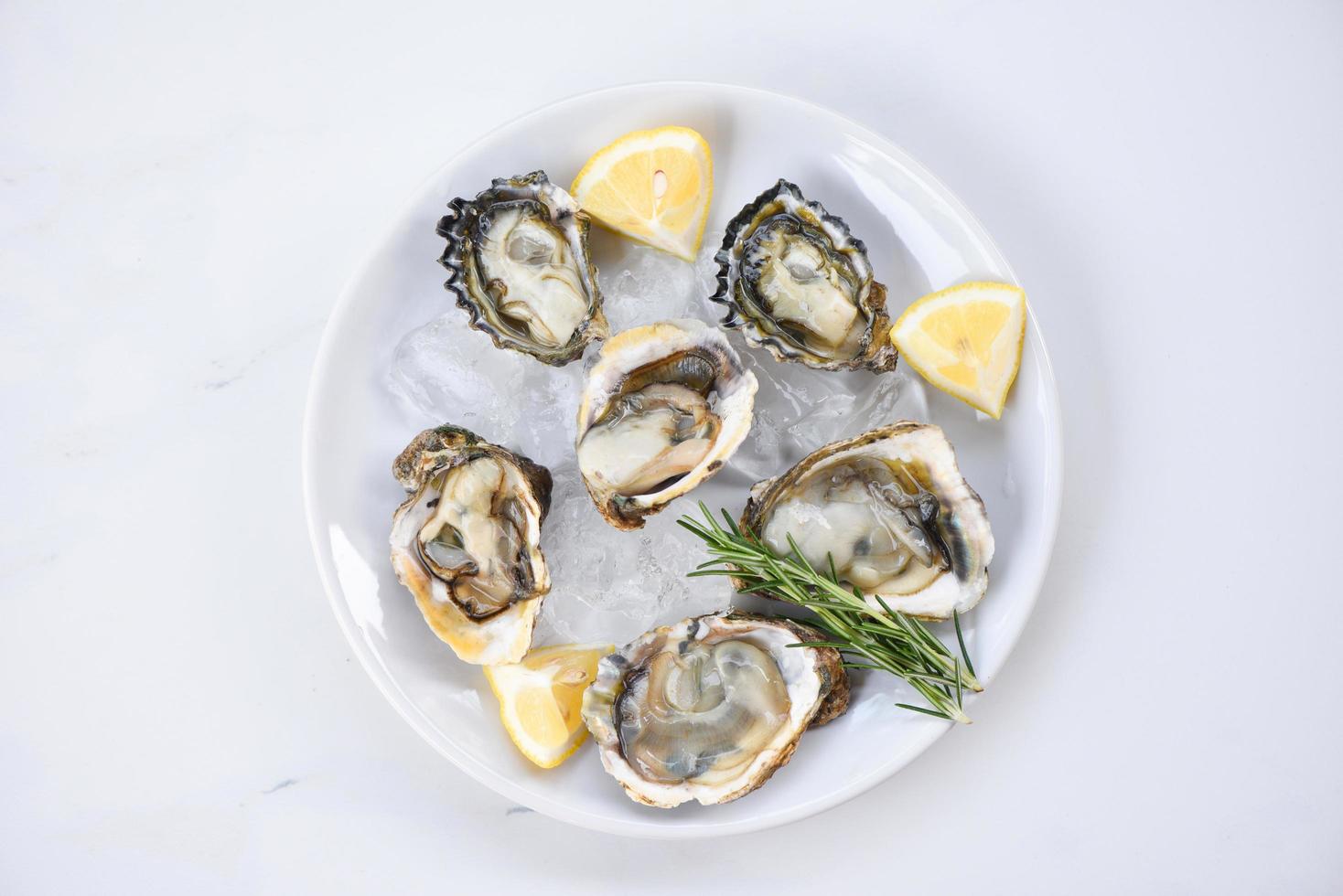 ostras frescas frutos do mar no fundo da chapa branca - concha de ostra aberta com ervas especiarias limão alecrim servido na mesa e gelo frutos do mar saudáveis jantar de ostras cruas no restaurante comida gourmet foto