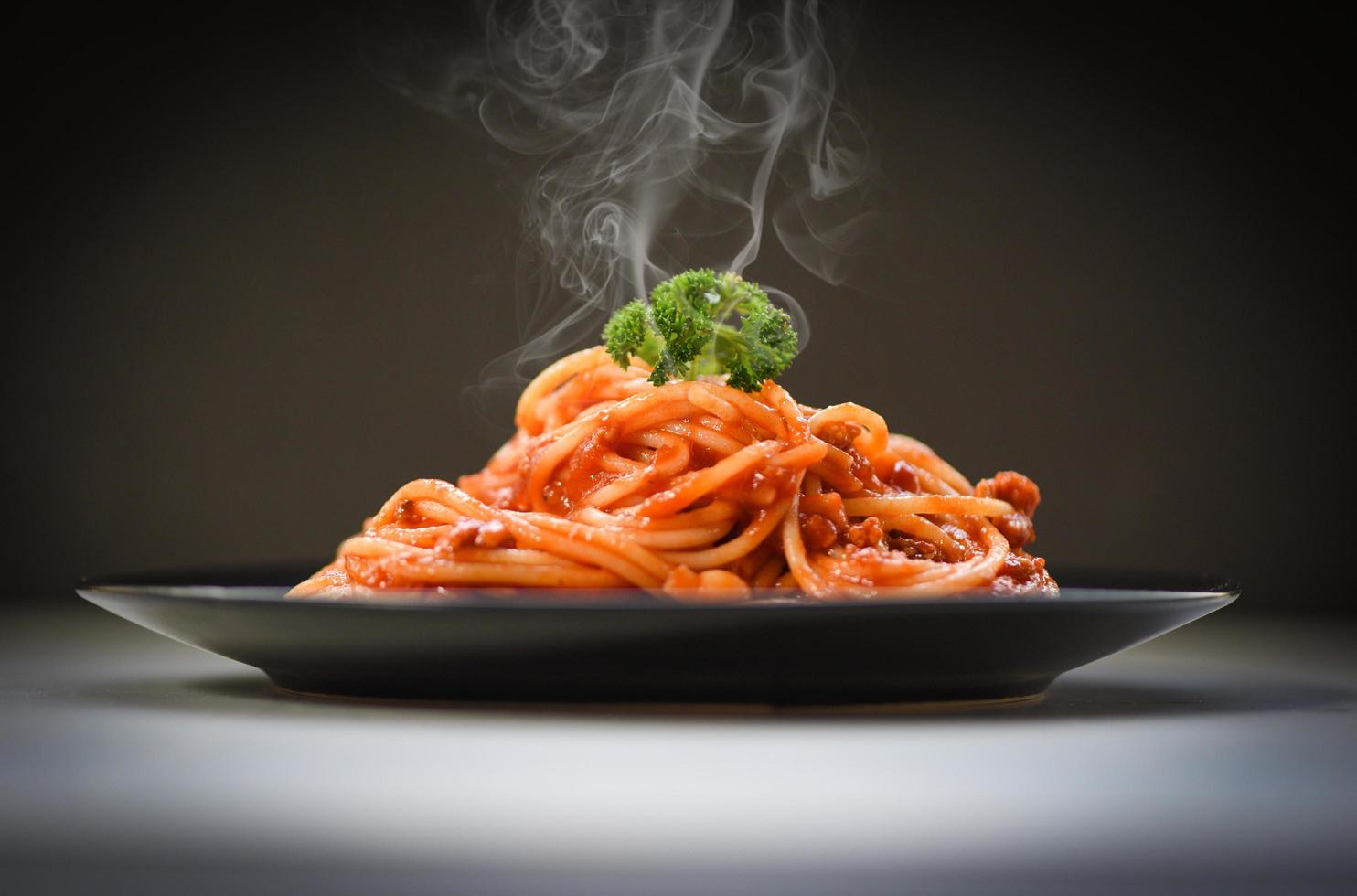 espaguete à bolonhesa em fundo preto espaguete italiano macarrão servido na chapa preta com molho de tomate e salsa no restaurante comida italiana e menu foto