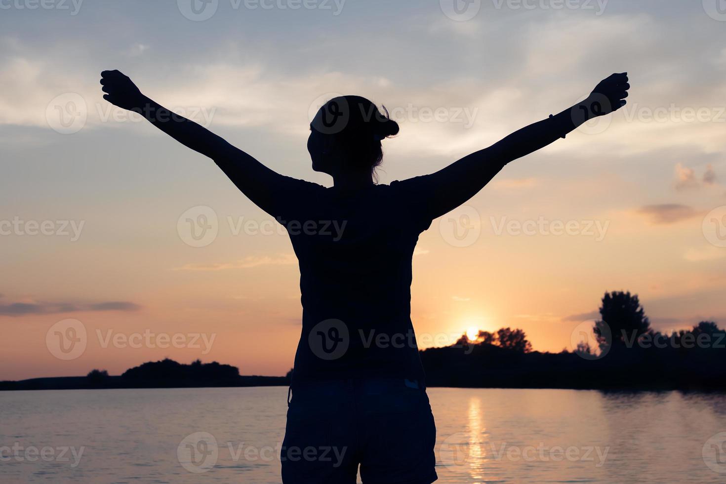 silhueta de mulher despreocupada com os braços estendidos na praia ao pôr do sol. foto