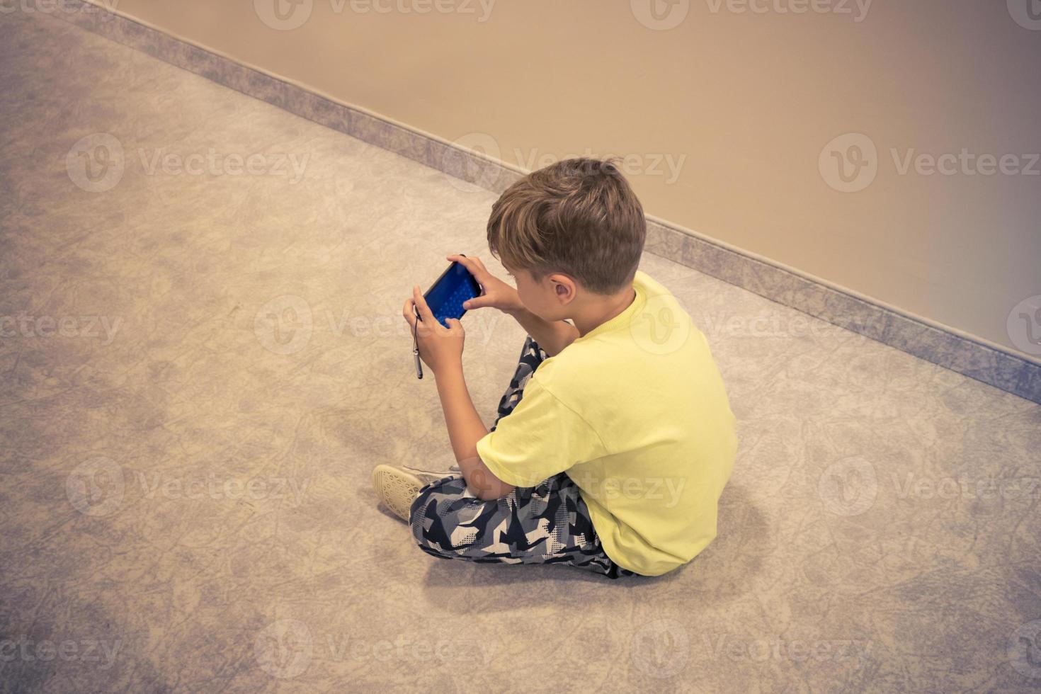 menino usando telefone inteligente enquanto está sentado no chão. foto