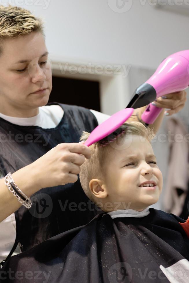 garotinho secando o cabelo depois de um corte de cabelo no salão. foto