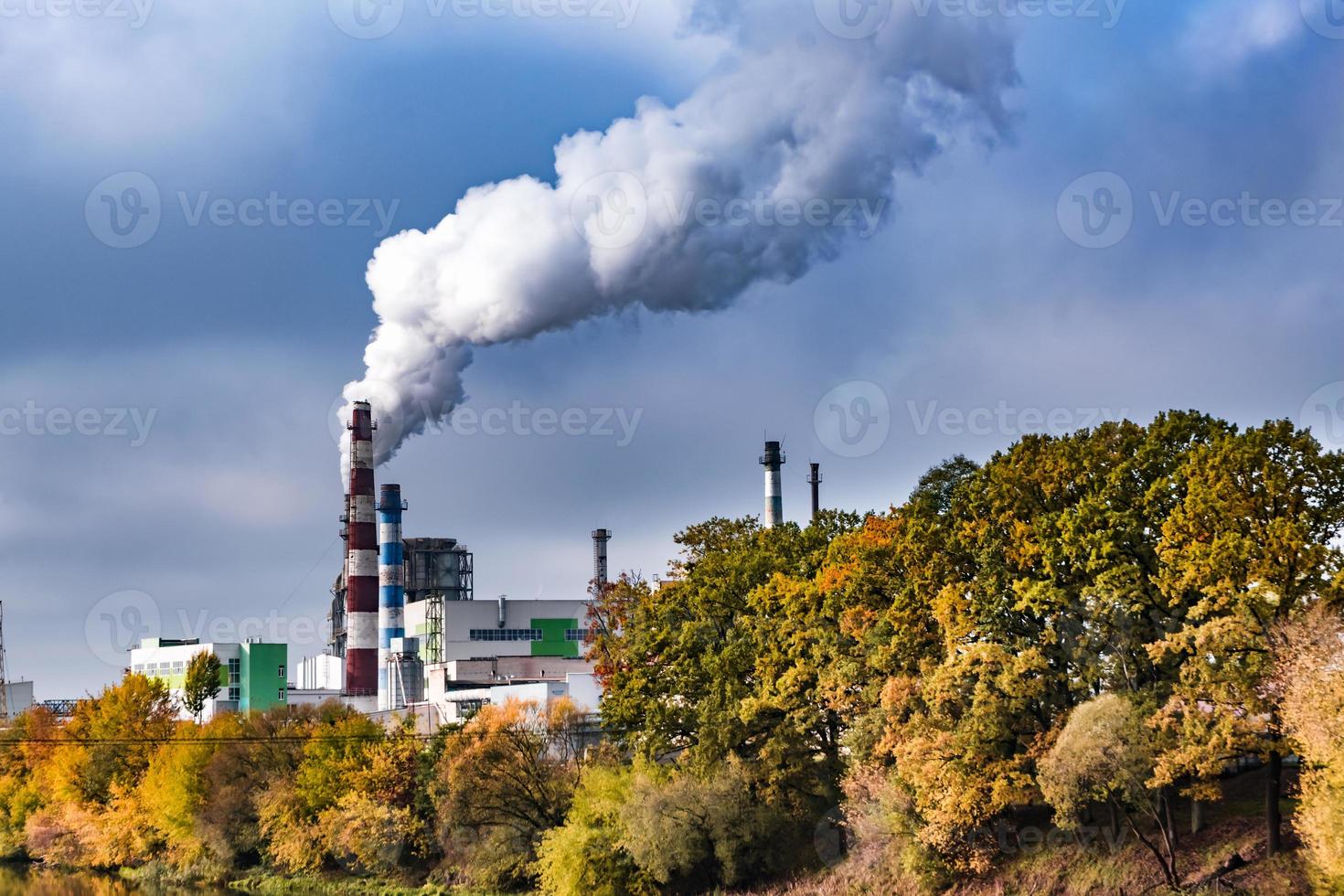 tubos de marcenaria empresa planta serraria perto do rio com árvores de outono vermelho amarelo. conceito de poluição do ar. paisagem industrial poluição ambiental resíduos de usina termelétrica foto