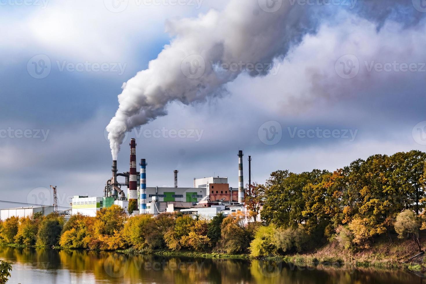 tubos de marcenaria empresa planta serraria perto do rio com árvores de outono vermelho amarelo. conceito de poluição do ar. paisagem industrial poluição ambiental resíduos de usina termelétrica foto