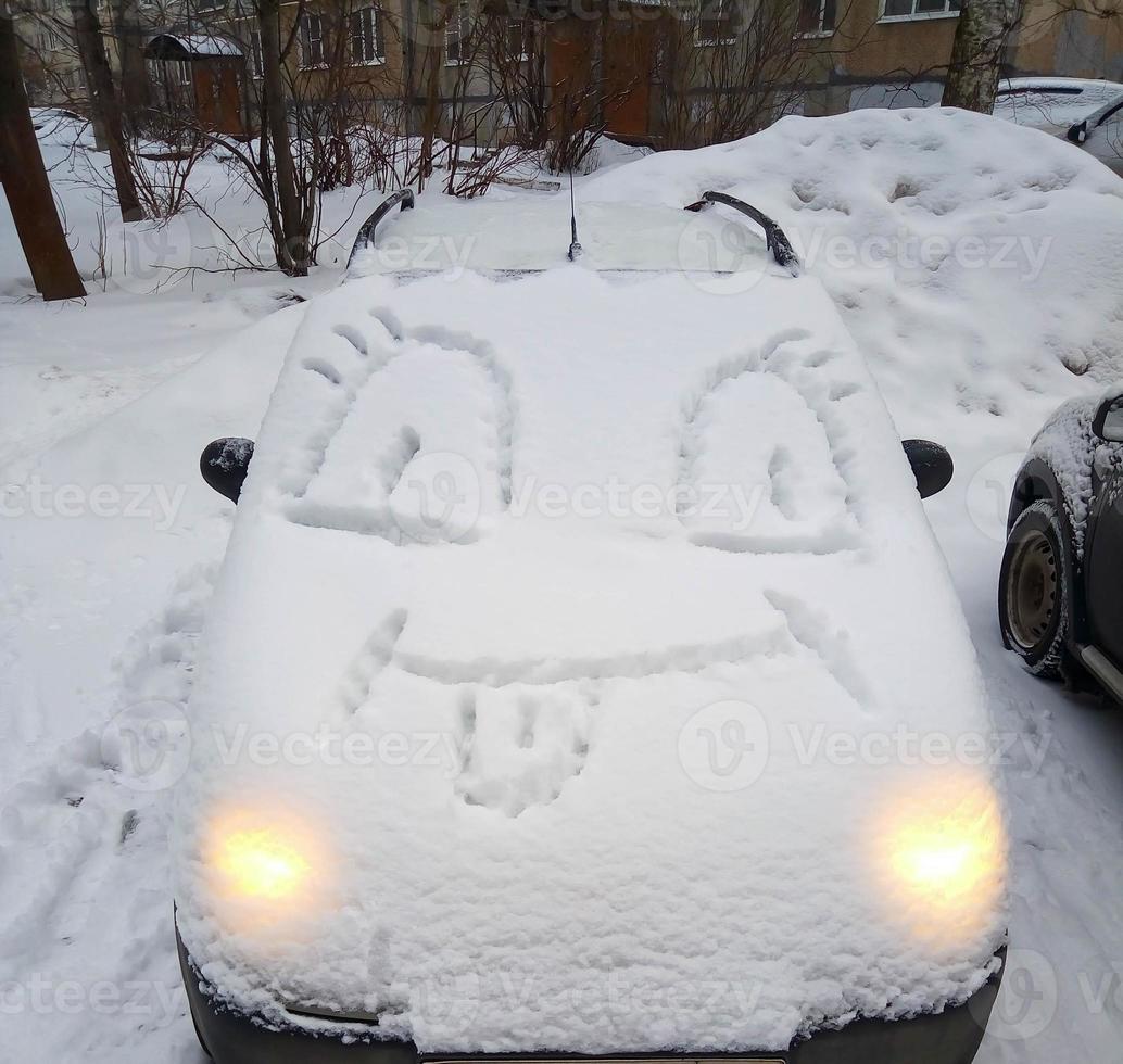 um carro coberto de neve, com uma cara engraçada no capô. diversão de inverno foto