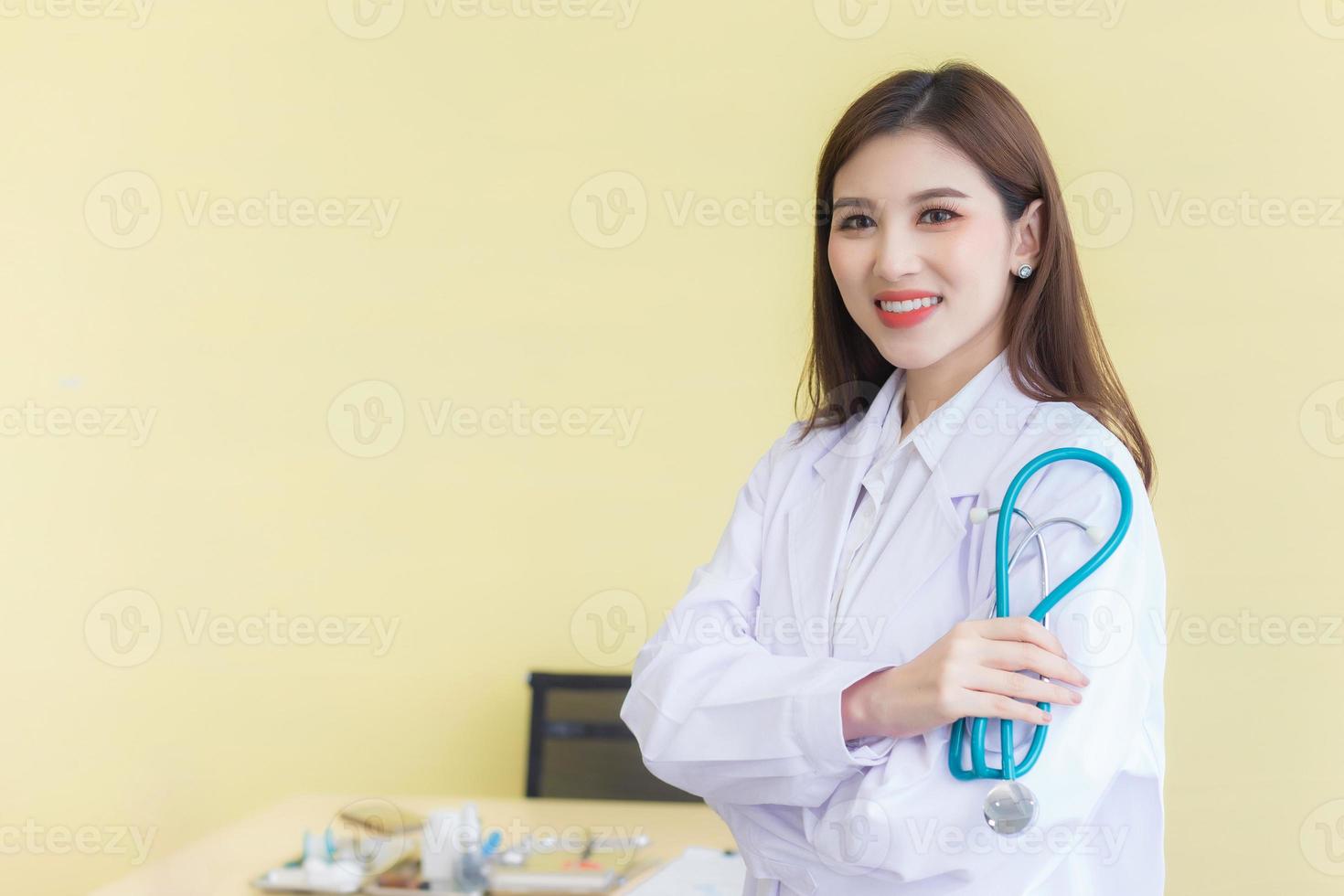 médico jovem bela mulher asiática em pé com os braços cruzados feliz e sorriso no hospital. vestindo uma túnica branca e estetoscópio foto