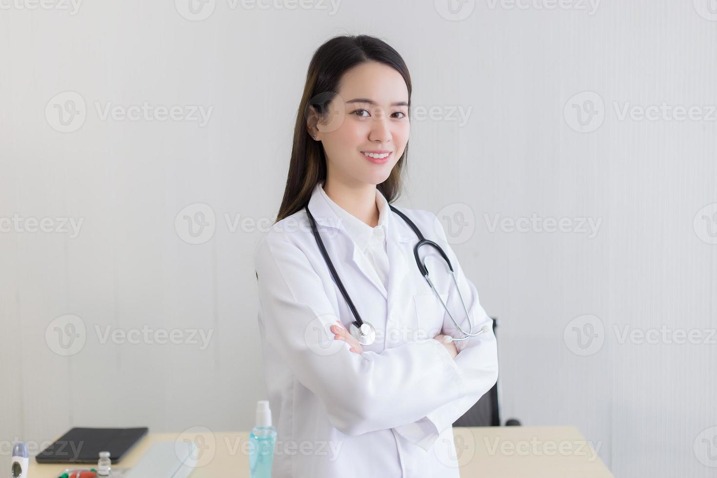 médico jovem bela mulher asiática em pé com os braços cruzados feliz e sorriso no hospital. vestindo uma túnica branca e estetoscópio foto