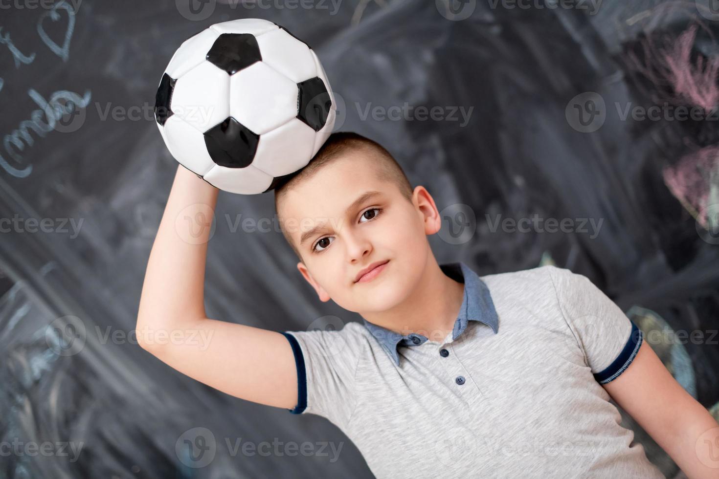 menino feliz segurando uma bola de futebol na cabeça foto