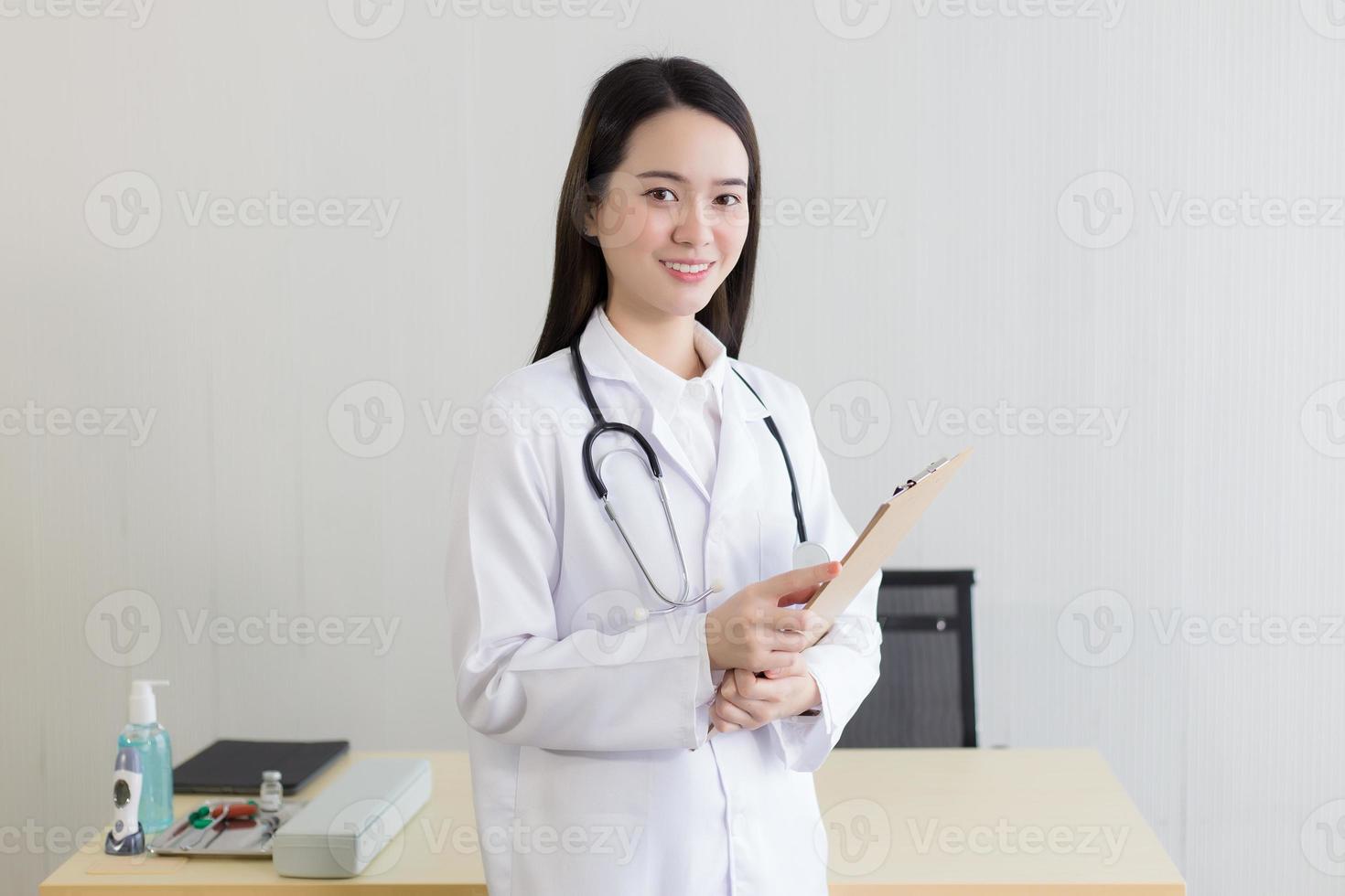 jovem e bela médica asiática trabalhando no hospital. ela usa uma túnica branca e estetoscópio e segura uma prancheta nas mãos. foto