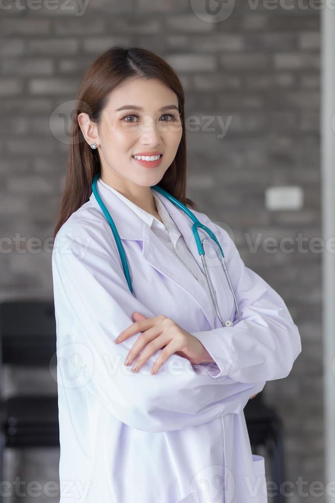 médica profissional mulher asiática em pé com os braços cruzados feliz e sorriso no hospital. vestindo uma túnica branca e estetoscópio foto