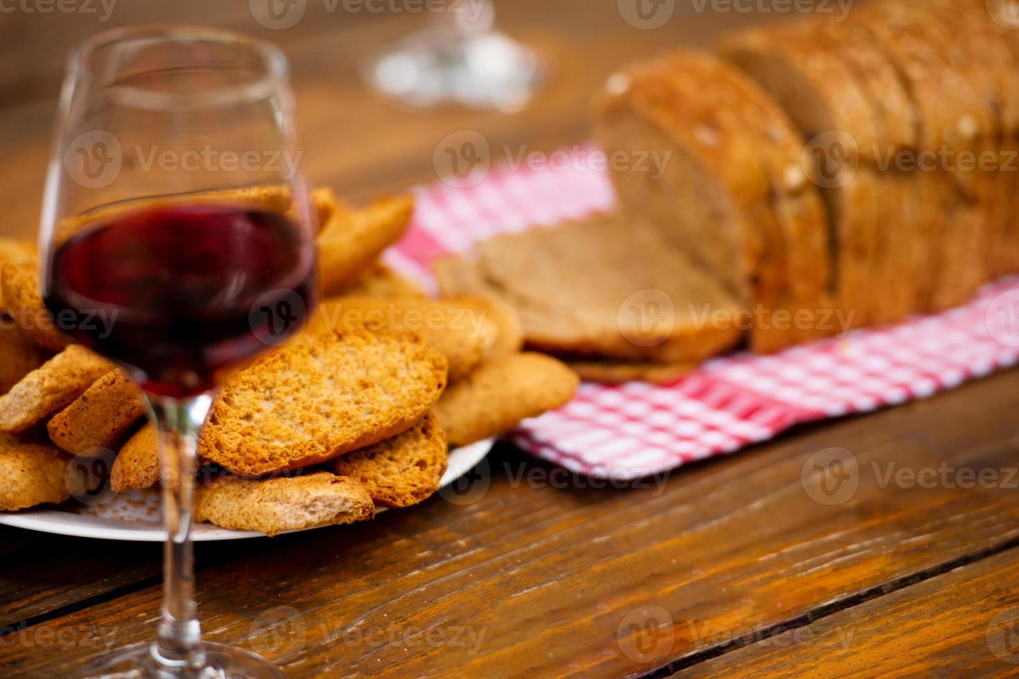 copo de vinho tinto e pão torrado na mesa de madeira foto