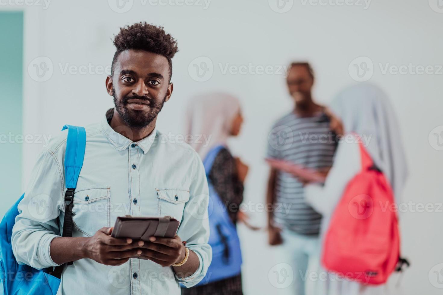 estilo de vida universitário bonito jovem estudante segurando um computador tablet e sorrindo em pé contra a universidade com seus amigos tem uma reunião de equipe em segundo plano. foto de alta qualidade