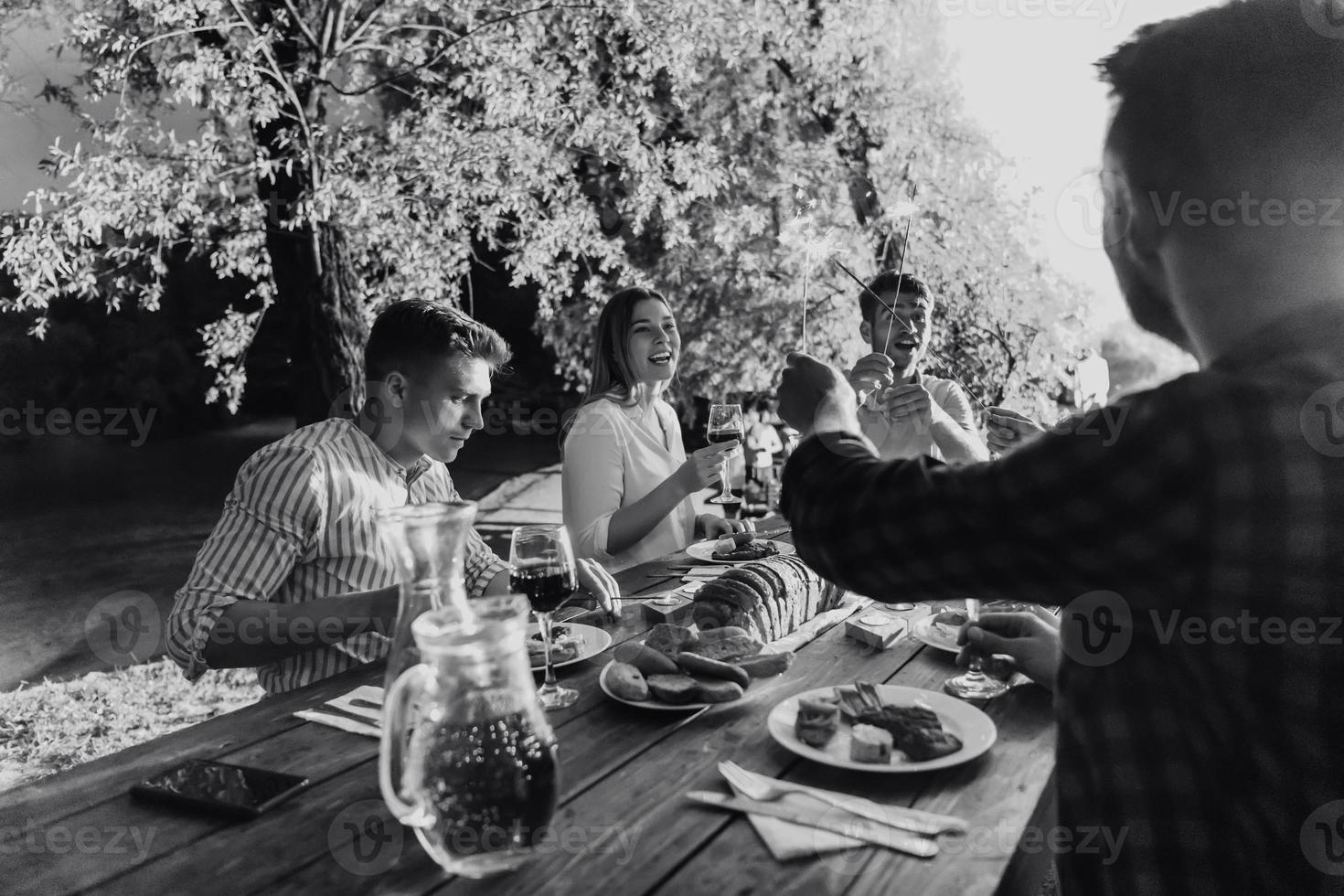 amigos comemorando férias de férias usando aspersores e bebendo vinho tinto enquanto faz piquenique com jantar francês foto